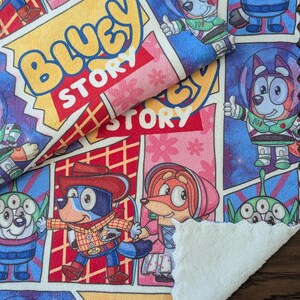 May include: A colorful Bluey Story themed blanket with comic book style panels. The blanket features cartoon characters in various outfits, including a cowboy and astronaut. The text "Bluey Story" is prominently displayed in a yellow bubble.