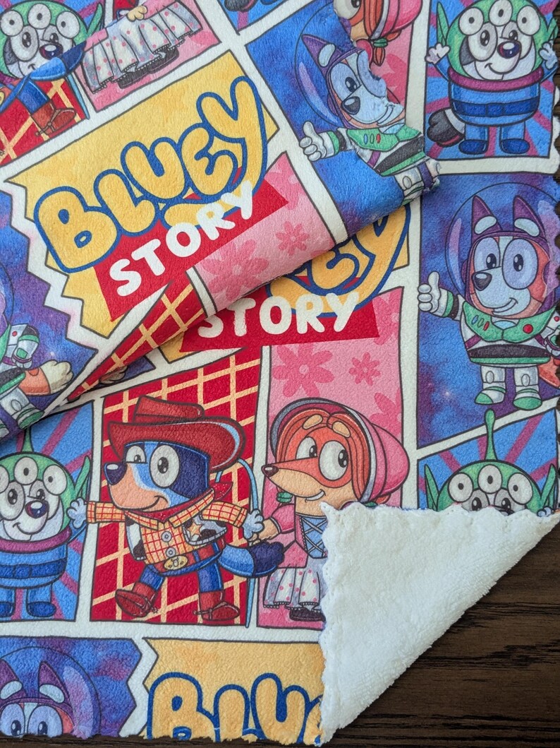 May include: A colorful Bluey Story themed blanket with comic book style panels. The blanket features cartoon characters in various outfits, including a cowboy and astronaut. The text "Bluey Story" is prominently displayed in a yellow bubble.