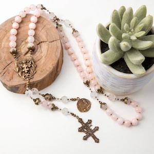he Saint Joan of Arc rosary is draped over a small tree ring with a 3" potted plant beside it.