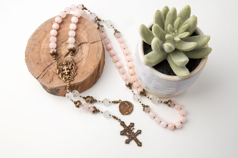 he Saint Joan of Arc rosary is draped over a small tree ring with a 3" potted plant beside it.