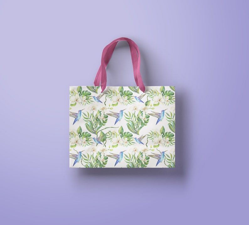 May include: A white tote bag with pink handles features a repeating pattern of blue hummingbirds, white flowers, and green leaves.
