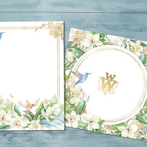 May include: Two white cards with gold frames and floral designs. The cards feature white orchids, green leaves, and blue hummingbirds. One card has a gold circle with the initials "WW" in the center.