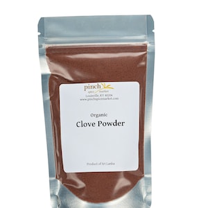 May include: A silver resealable pouch filled with organic clove powder. The pouch has a label that reads "Pinch Spice Market, Louisville, KY 40206, www.pinchspicemarket.com, Organic Clove Powder, Product of Sri Lanka."