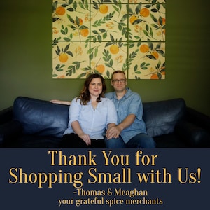 May include: A couple smiles and sits on a dark blue couch in front of a wall with a floral print. The text "Thank You for Shopping Small with Us! -Thomas & Meaghan your grateful spice merchants" is displayed below the couple.