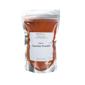 May include: A silver resealable pouch filled with red organic cayenne powder. The pouch has a white label with the text "pinch spice market Louisville, KY 40203 www.pinchspicemarket.com Organic Cayenne Powder Product of Sri Lanka".