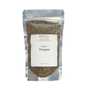 May include: A silver resealable pouch filled with dried organic oregano. The pouch has a white label with the text "pinch spice market" in gold lettering, "Louisville, KY 40206", "www.pinchspicemarket.com", "Organic Oregano", and "Product of Albania".