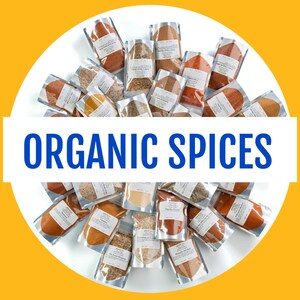 May include: A variety of organic spices in small pouches, labeled with their names. The pouches are arranged in a circle on a white surface, with the text "ORGANIC SPICES" in blue letters across the center.