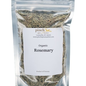 Può includere: Un sacchetto trasparente sigillato di rosmarino biologico. La busta ha un'etichetta bianca con la scritta "Organic Rosemary" e il logo Pinch Spice Market. Il prodotto è della Tunisia.