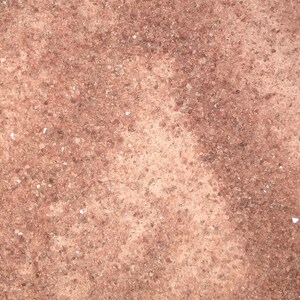 May include: Close-up of a reddish-brown textured surface with a grainy appearance. The surface has a slightly uneven texture with a subtle variation in color.