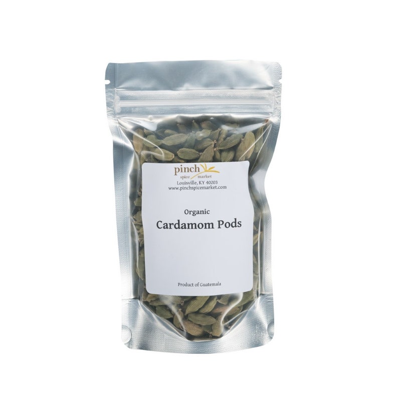 May include: A silver resealable pouch filled with organic cardamom pods. The pouch has a white label with the text "Pinch Spice Market" and "Organic Cardamom Pods".