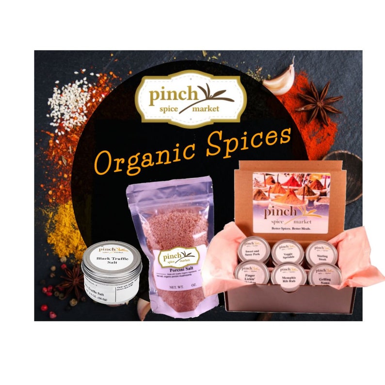 Pode incluir: Um conjunto de especiarias org&acirc;nicas numa caixa castanha com um r&oacute;tulo rosa e branco que diz "pinch spice market". A caixa cont&eacute;m seis pequenos frascos de especiarias, incluindo sal de trufa negra, sal de cogumelo porcini e especiarias para grelhar. A caixa &eacute; rodeada por v&aacute;rias especiarias, incluindo flocos de pimenta vermelha, sementes de s&eacute;samo e anis estrelado.