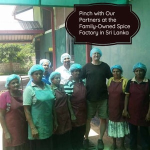 May include: A group of people wearing blue hairnets and aprons stand in a spice factory in Sri Lanka. The text "Pinch with Our Partners at the Family-Owned Spice Factory in Sri Lanka" is displayed in a black frame.
