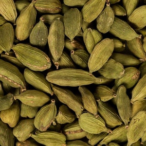 May include: A close-up image of a pile of green cardamom pods. The pods are arranged in a random pattern, showing their natural texture and color.