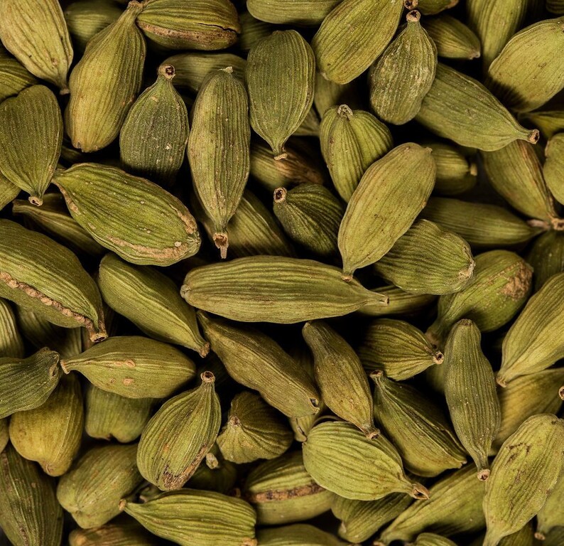 May include: A close-up image of a pile of green cardamom pods. The pods are arranged in a random pattern, showing their natural texture and color.