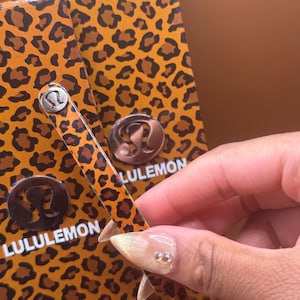 May include: A leopard print box and a matching accessory with the word LULULEMON. The accessory has a silver metal detail with the Lululemon logo. The box and accessory have a brown and tan spotted pattern.