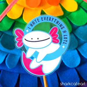 Puede incluir: Una pegatina con un ajolote blanco con branquias rosas y cola azul, nadando en círculo. El ajolote sonríe y la pegatina dice "¡Odio todo mucho!" en un círculo blanco con contorno negro.
