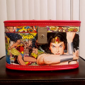 May include: A red, rectangular, hinged box with a Wonder Woman comic book design. The box has a lock and keyhole. The design features Wonder Woman in a red, blue, and gold costume.