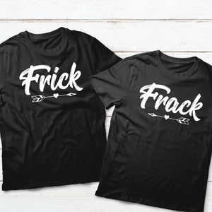 May include: Two black t-shirts with white text. One shirt says "Frick" and the other says "Frack". Both shirts have a white arrow with a heart. The shirts are on a white wooden surface.
