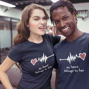 May include: A couple wearing matching navy blue t-shirts with a white heartbeat graphic and the text "my heart belongs to him" and "my heart belongs to her".