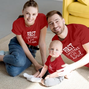 May include: A family of three wearing matching red shirts with white text. The shirts say "First Christmas as Mom", "First Christmas as Dad", and "First Christmas".