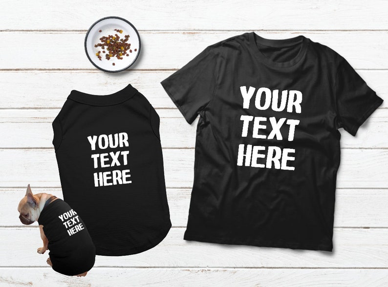 May include: Black t-shirts and dog shirts with the text "YOUR TEXT HERE" in white. A small dog is wearing a matching shirt. A bowl of dog food is in the background.
