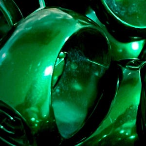 Può includere: Primo piano astratto di più oggetti verde smeraldo lucidi. Le forme sono curve e riflettenti, con luci e ombre che creano profondità. L'effetto complessivo è una composizione vibrante e strutturata.