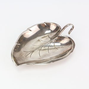 May include: A silver leaf-shaped dish with a handle. The dish is decorated with a leaf design.