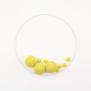 May include: A white metal hoop with yellow felt balls of various sizes hanging from it. The hoop is on a white background.