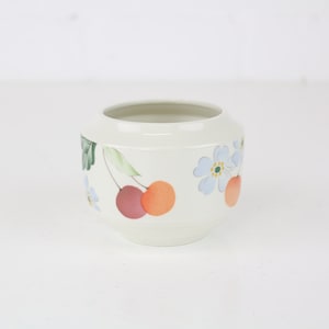 Könnte beinhalten: Weiße Keramik Schale mit einem Blumendesign mit Kirschen, Blättern und Blumen in Rot-, Orange-, Grün-, Blau- und Gelbtönen.