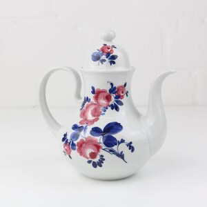 Könnte beinhalten: Weiße Porzellan-Kaffeekanne mit floralem Design mit rosa Rosen und blauen Blättern. Der Deckel hat ein florales Design.