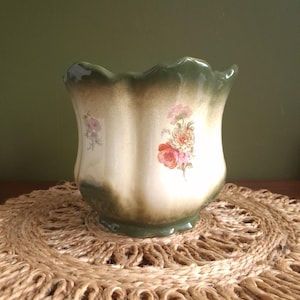 May include: A ceramic planter with a scalloped rim and a cream-coloured body featuring a gradient dark green finish at the top and bottom. The exterior is decorated with small, colourful floral decals of roses and other blossoms in pink and orange.