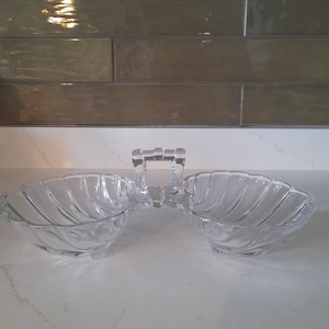 May include: A clear glass serving dish with two bowls and a handle. The bowls are shaped like seashells and have a ribbed design.