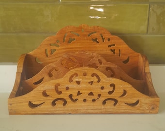 May include: A wooden desk organizer with a natural finish. The organizer has three compartments and decorative cut-out designs. The top edge has a scalloped shape. The wood grain is visible.