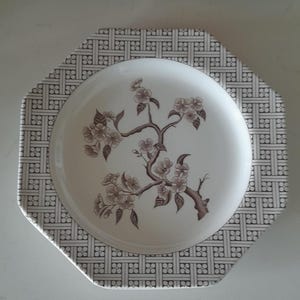 Könnte beinhalten: Eine weiße ovale Servierplatte mit braunem Blumendesign und einem schwarzen und weißen gewebten Muster an der Kante.