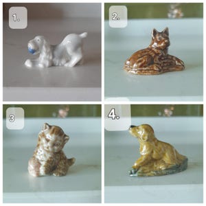 May include: Four ceramic dog and cat figurines. The first is a white dog with a blue ball. The second is a brown dog lying down. The third is a brown and tan kitten. The fourth is a tan dog looking up.
