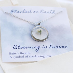 May include: A silver necklace with a round pendant containing a preserved baby's breath flower. The card reads "Planted on Earth, Blooming in Heaven. Baby's Breath: A symbol of everlasting love."