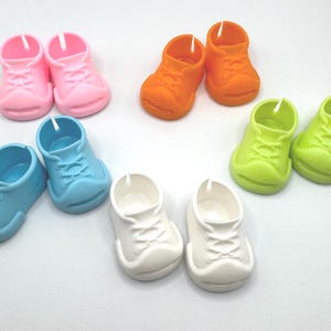 May include: A collection of colorful miniature toy sneakers in pink, orange, light blue, green, and white. The shoes are arranged in pairs, showcasing their small size and playful design. These plastic shoes are likely for dolls or other toys.