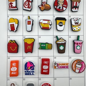 May include: A collection of colorful food-themed charms, including fast food logos like KFC, McDonald's, Taco Bell, and Starbucks. The charms are made of plastic and feature various food items and brand logos. The collection includes a variety of colors and designs.