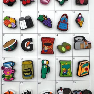 May include: A collection of colorful shoe charms featuring various designs. Includes cherries, a cupcake, a salt and pepper shaker, a bunch of grapes, an apron, an ice cream cone, a Gatorade logo, a bag of chips, an avocado, a stack of teacups, a jar of pickles, a golf club, and a hamburger.