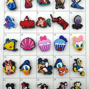 May include: A collection of colorful shoe charms featuring various cartoon characters and designs. Includes characters like Elsa, Anna, Ariel, Mickey Mouse, and Donald Duck. The charms are made of a rubbery material and are designed to be attached to shoes.