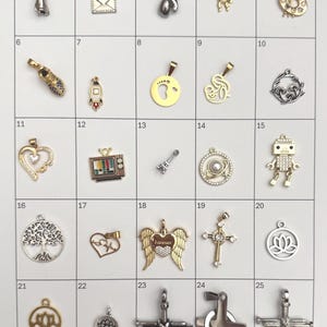 May include: A collection of 25 small metal charms in various shapes, including a boxing glove, a heart, a robot, a cross, and a tree of life. The charms are gold and silver-toned, with some featuring gemstones or intricate designs.