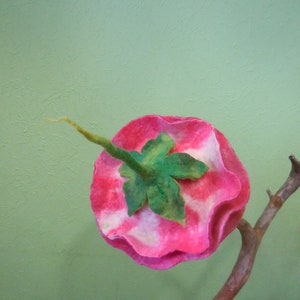 May include: A pink and white felt flower with a green leaf, attached to a brown branch.