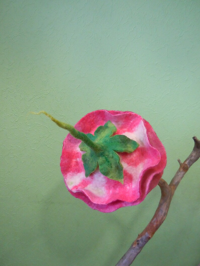 May include: A pink and white felt flower with a green leaf, attached to a brown branch.