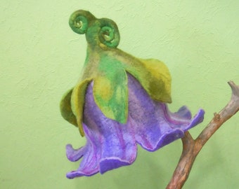 May include: A purple and green felt flower with a curled stem, attached to a brown branch. The flower is made of wool felt and has a realistic appearance.