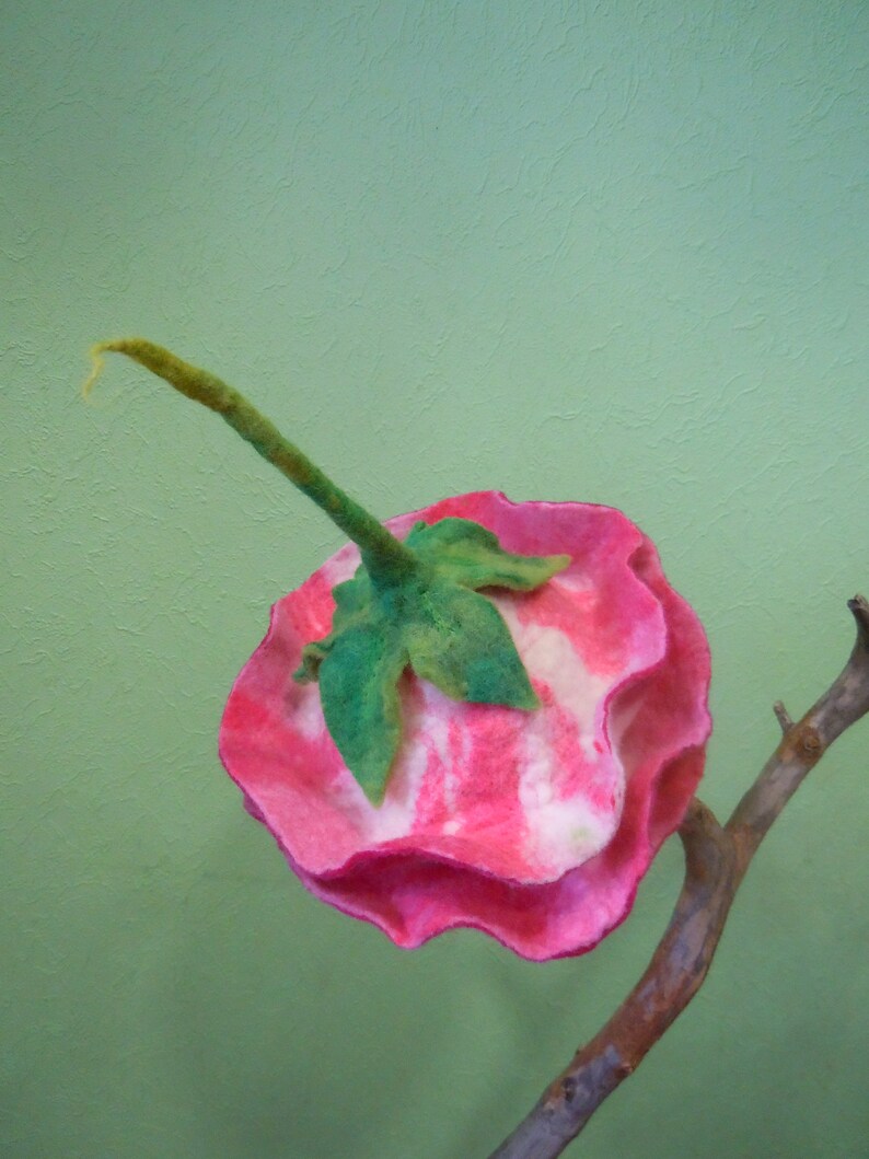 May include: A pink and white felt flower with a green stem. The flower is shaped like a rose and has a ruffled edge.