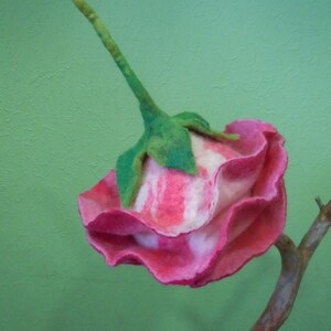 May include: A pink and white felt flower with green leaves and a stem. The flower is shaped like a rose and has a ruffled edge.