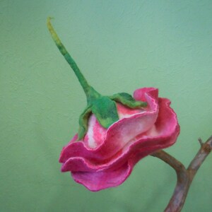 May include: A pink and white felt rose with green stem and leaves, attached to a brown branch.