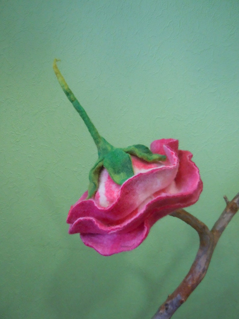 May include: A pink and white felt rose with green stem and leaves, attached to a brown branch.