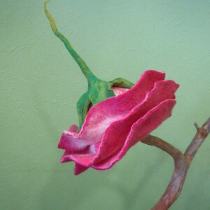 May include: A pink felt flower with green stem and leaves, attached to a brown branch.