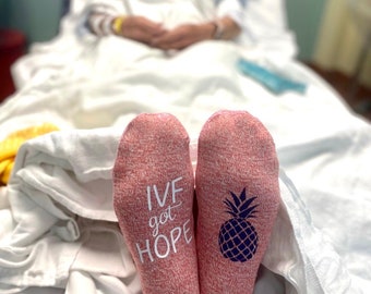 May include: A pair of pink socks with a pineapple design on one sock and the text "IVF got HOPE" on the other sock.